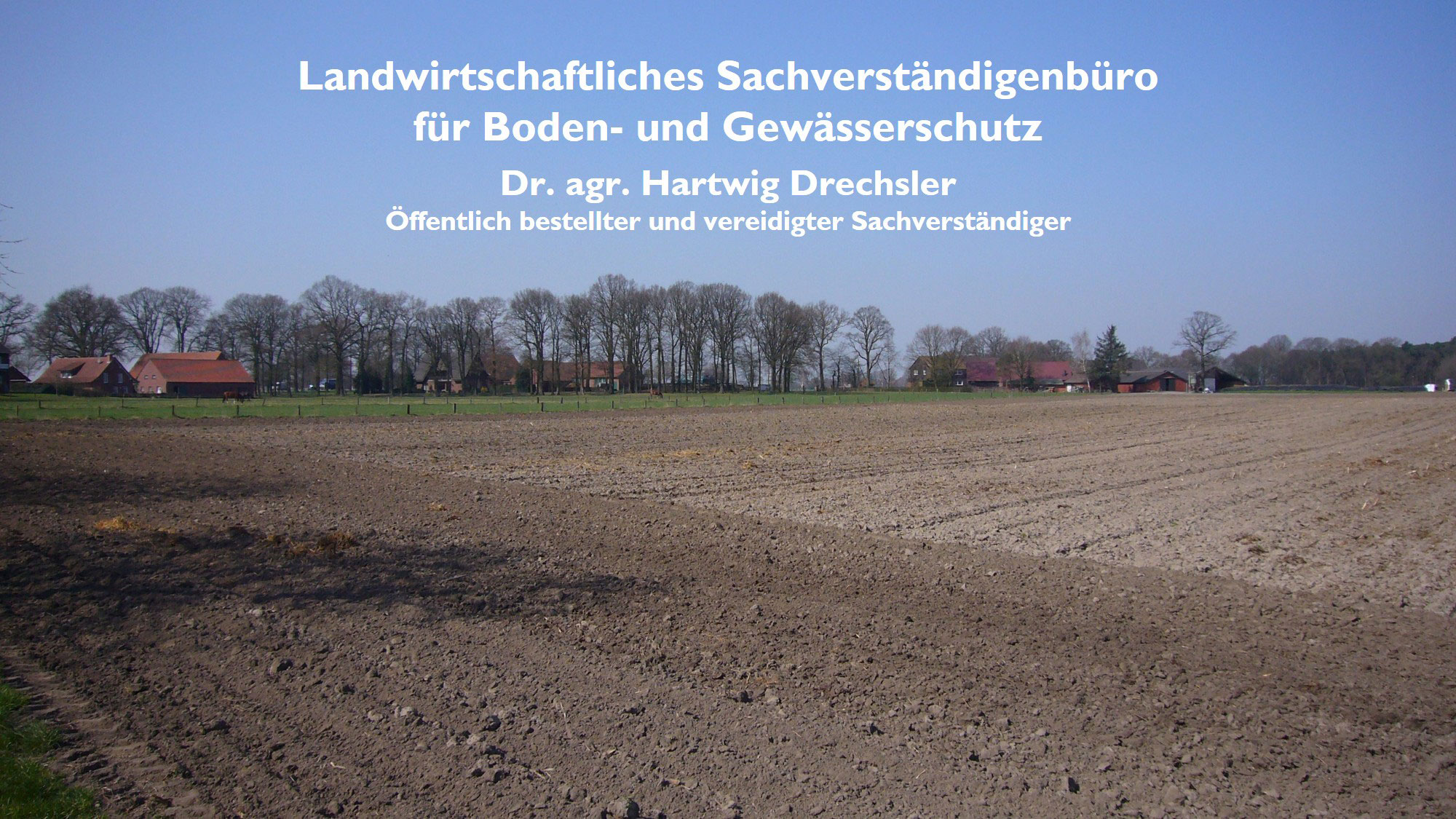 Ackerfläche mit Wiese und Gehöft im Hintergrund